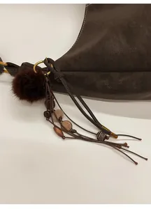 Detail of faux fur pom-pom charm with wooden beads and tassels on a brown leather bag