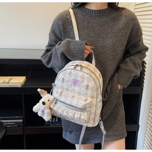 Détail du sac à dos crème avec écusson cerise, dentelle et breloque chien peluche