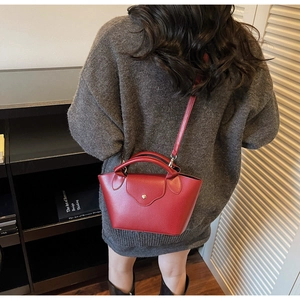 Detail of red lychee textured dumpling handbag with metal snap button and handle