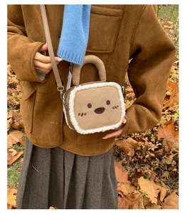 Outdoor shot of a brown plush square bag with white fleece trim and cute smile face