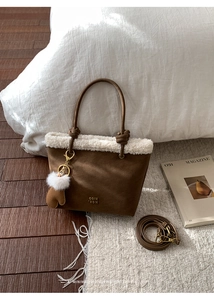 Detail of suede bucket bag with white faux fur trim, gold logo, and plush pompom accessory