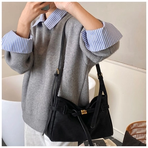 Détail du sac cabas en similicuir noir avec boucle dorée sur fond de pull gris