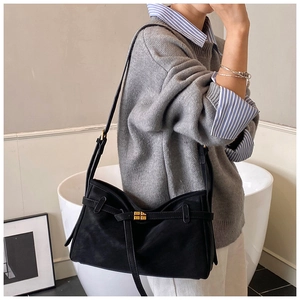 Detail view of large black matte shoulder bag featuring elegant golden cross-lock and strap