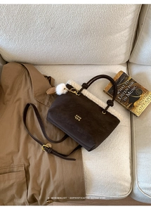 Detail of suede bucket bag with faux shearling trim and plush ball on a white sofa
