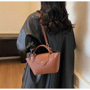 Brown leather dumpling bag with retro metal clasp shown on model's shoulder in studio