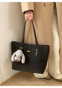 Detail of dark textured tote bag with plush rabbit charm and gold hardware accents