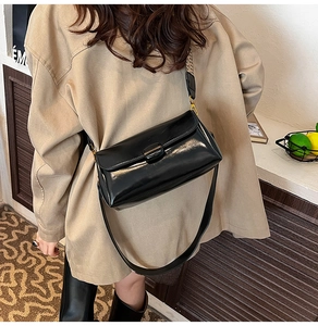 Detail shot of a black glossy PU leather crossbody bag with a sleek metal buckle design
