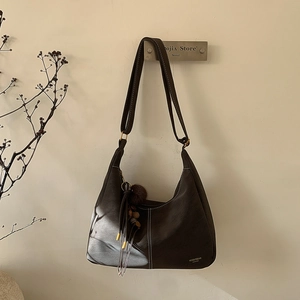 Detail of dark brown leather hobo bag featuring white contrast stitching and fur pompom