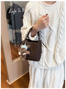 Detail of coffee brown pebble leather bucket bag with cute plush bear charm accessory