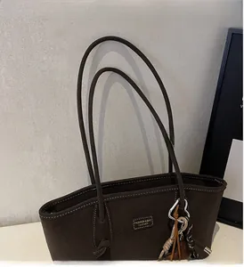 Détail du sac cabas mat marron foncé avec coutures contrastées et écusson en cuir déco