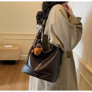 Detail view of dark brown oil-wax leather tote bag with a cute bear charm and woven cord