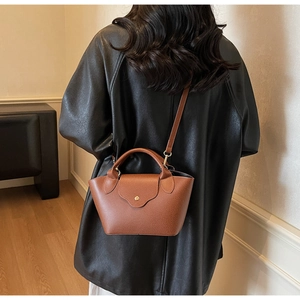 Detail of caramel brown leather handbag showing sleek top handle and golden buckle clasp
