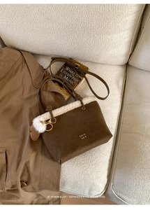 Close-up of brown suede bucket bag featuring faux shearling trim and a white fur charm