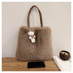 Detail of camel plush tote bag with woven brown leather handles and a cute bear charm