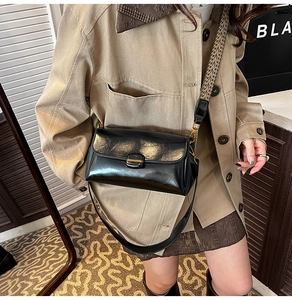 Detail of black glossy shoulder bag with vintage patterned wide strap and gold buckle