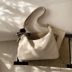 Close-up of cream leather dumpling bag with brown fur ball charm on rattan surface