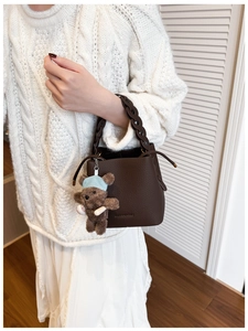 Detail of dark brown leather bucket bag with braided handle and cute teddy bear charm