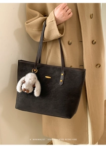 Detail of black suede tote bag with golden logo and a cute bunny plush charm