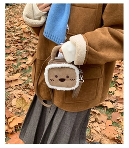 Detail of a brown plush crossbody bag with cartoon embroidery on an autumn leaf background