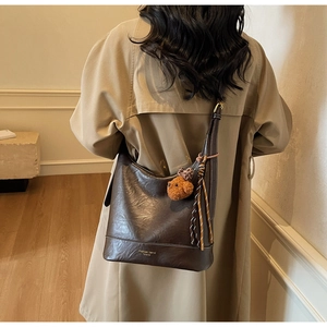 Close-up of dark brown tote bag with woven drawstring detail and a plush bear charm