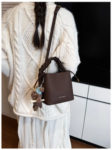 Détail du sac seau en cuir marron foncé avec poignée tressée et breloque ours en peluche