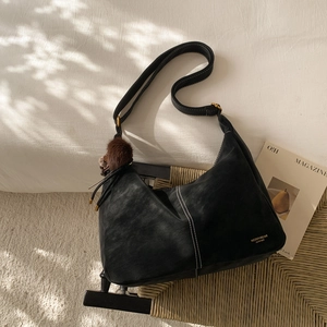 Detail of black leather tote bag featuring white stitching and gold brand logo