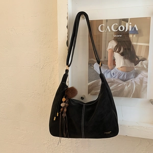 Detail of black suede hobo bag with contrast stitching and decorative tassel charm