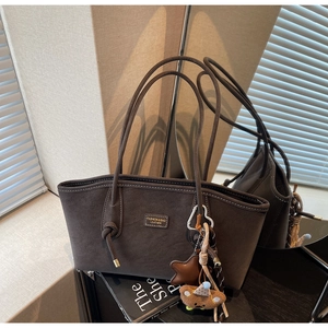 Détail d'un sac cabas en daim mat foncé avec des bretelles nouées et des breloques mignonnes