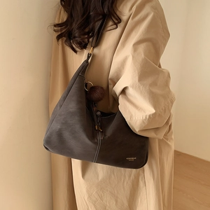 Close-up of brown hobo bag with contrast stitching and plush pompom charm detail
