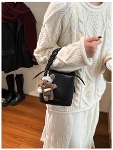 Detail of black lychee grain bucket bag with chain handle and cute teddy bear charm