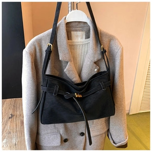 Détail d'un sac cabas vintage en cuir noir mat avec boucle dorée sur un manteau gris