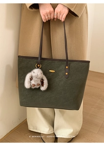 Deep green leather tote bag detail with plush bunny charm on a model in wool coat