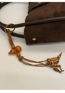 Gros plan du sac seau en daim marron avec des breloques en bois et des anneaux dorés