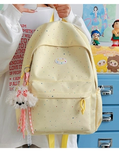Detail view of yellow canvas backpack with colorful dot patterns and plush dog charm