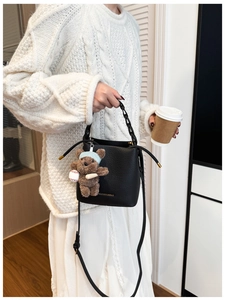 Detail of black pebbled leather bucket bag featuring a chain handle and cute bear charm