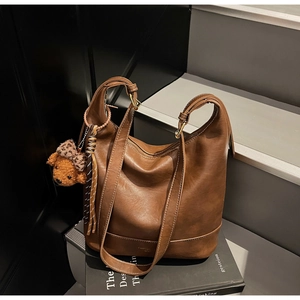 Detail of vintage brown leather tote bag with a cute bear charm on a modern staircase