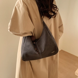 Detail of dark brown shoulder bag featuring contrast stitching and soft fur pompom charm