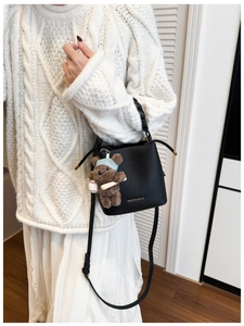 Detail of black pebbled leather bucket bag with gold logo and brown plush bear charm