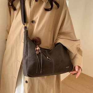 Detail of dark brown leather crossbody bag with white stitching and plush ball charm