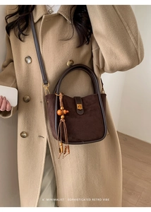 Détail du sac seau rétro en daim marron foncé avec pompon en perles de bois et fermoir doré