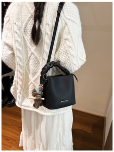 Détail du sac seau en cuir noir avec poignée tressée et pendentif ours en peluche