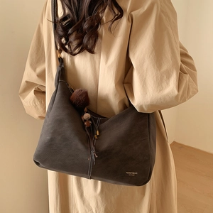 Detail of dark grey faux leather shoulder bag with pom-pom tassel on a khaki coat