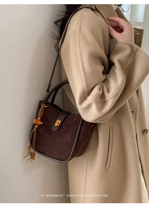 Détail d'un sac seau en daim marron avec fermoir tournant doré et pompon en perles de bois