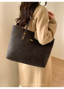 Close-up of a minimalist dark grey tote bag with gold stud details on a camel coat