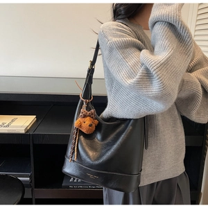 Close-up of black leather tote bag with a cute teddy bear charm and fashion trend logo