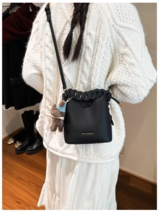 Detail of black lychee grain leather bucket bag with woven chain trim and bear charm