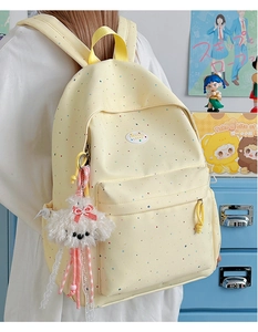 Detailed view of yellow polka dot backpack with a cute white puppy plush charm