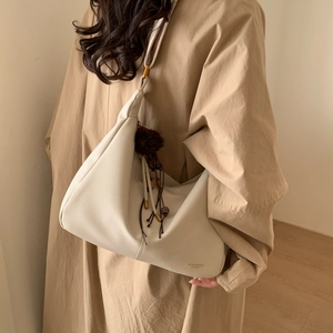Detail of hobo bag in cream leather with wood bead tassel and fur ball charm accessory
