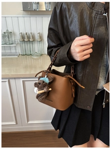 Detail of brown pebbled leather bucket bag with woven handle and plush bear charm