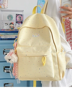 Close-up of yellow polka dot backpack with plush dog charm and multi-pocket design